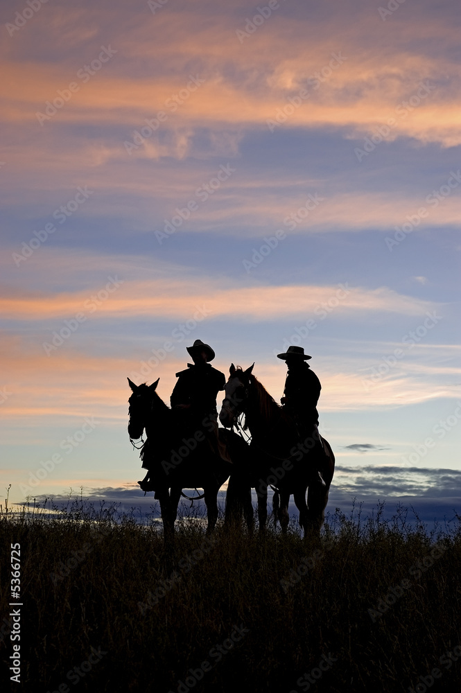 Cowboys silhouettes against a dawn sky. Horse ranch in Montana