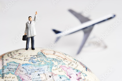 Business figurine on earth globe with toy airplane