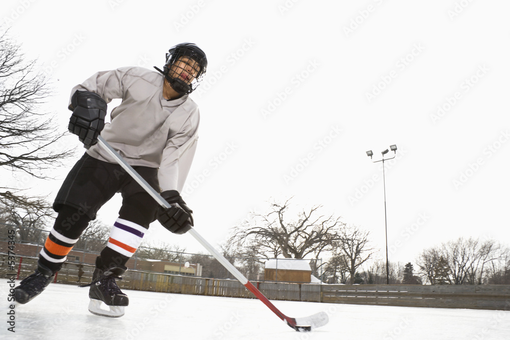 Obraz premium Boy in ice hockey uniform skating on ice rink moving puck.