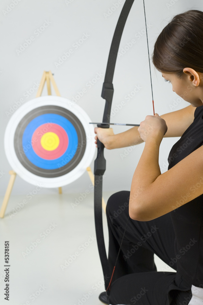 Fototapeta premium Young lady archer holding bow and taking aim at targer