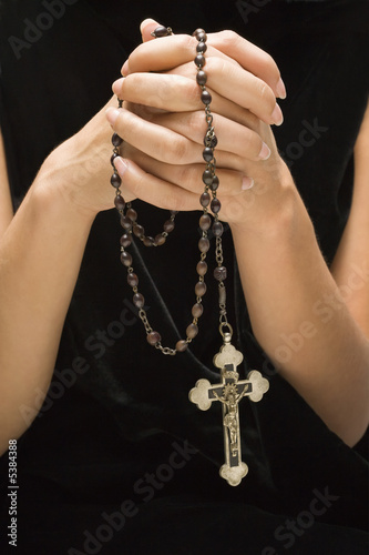 Woman holding rosary with hands clasped together.