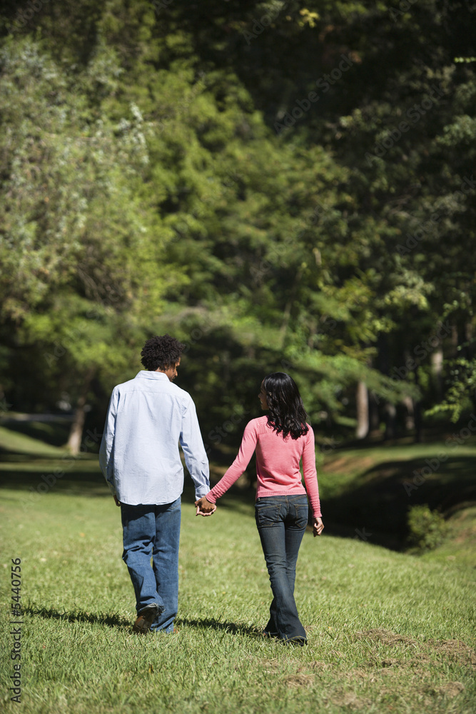 Couple holding hands walking and talking in park.