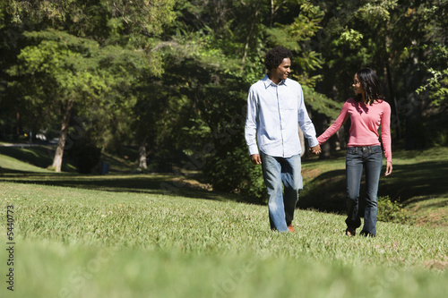 Smiling couple holding hands walking and talking in park.