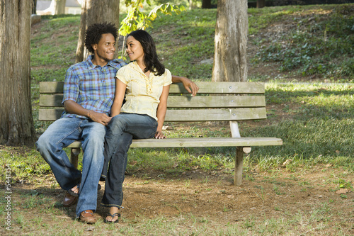 Happy smiling couple sitting on bench in park together.