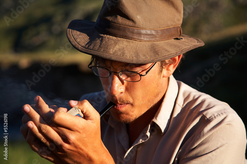 man in hat is smoking tobacco-pipe outdoors