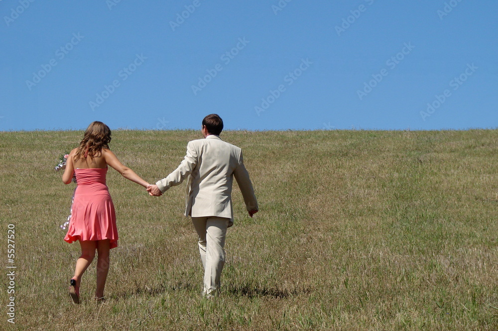 © fotosergio - Young couple walking in wide green field under blue sky © fotosergio - Young couple walking in wide green field under blue sky