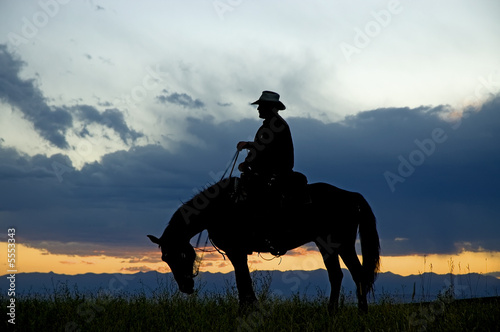 Cowboy on horseback silhouetted against dawn sky