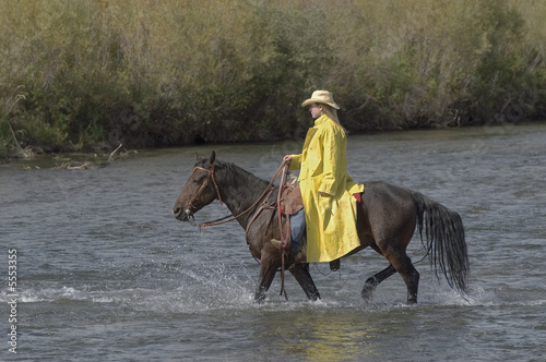 Cowgirl riding across river after the rain
