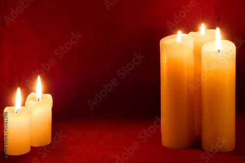 Five burning yellow-white candles on scarlet background