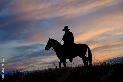 Cowboy on horseback back lit by the dawn sky photo
