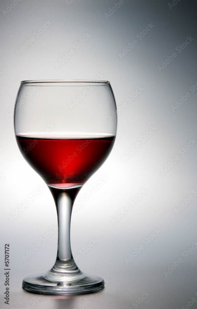 Footed glass of red wine over grey background Footed glass of red wine over grey background