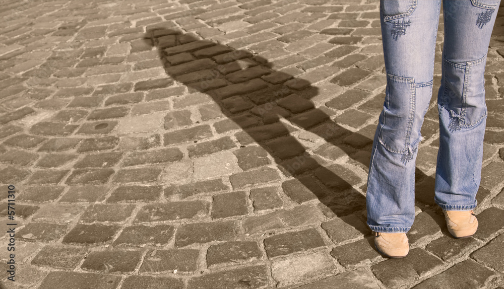 Legs in jeans casting a shadow on a pavement street. 
