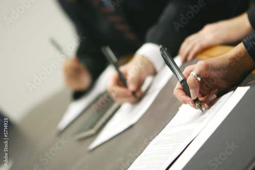 three hands holding pens signing document on table