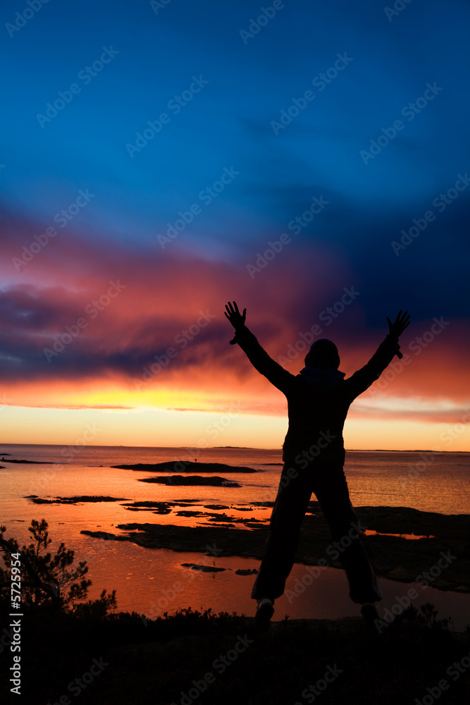 A person standing by the ocean raising their arms in celebration A person standing by the ocean raising their arms in celebration