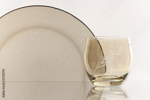 A glass beside a stack of white plates - on white background
