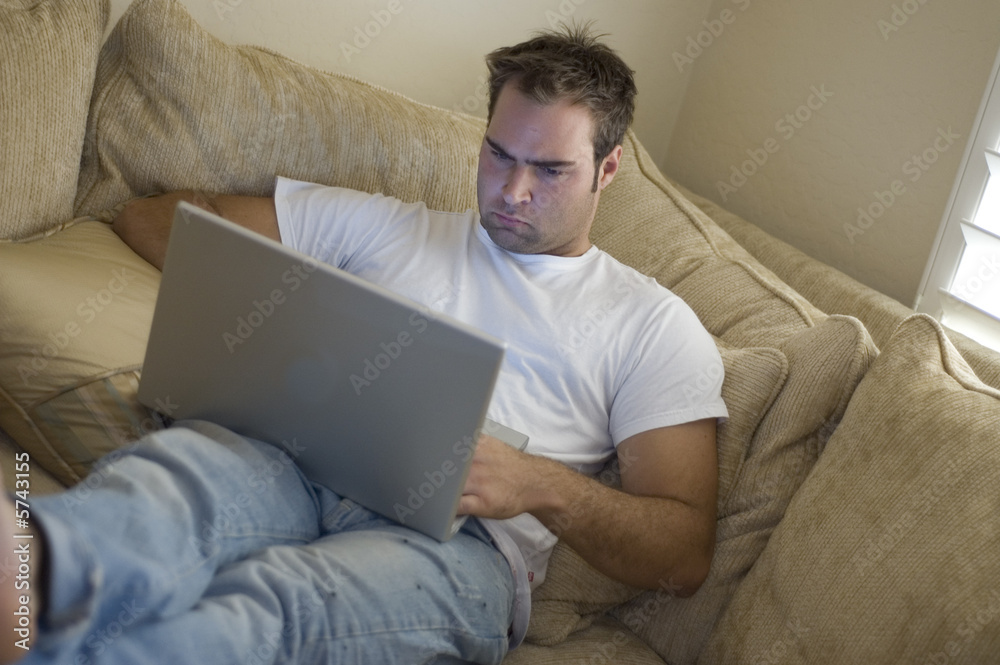 young man laying on sofa using laptop computer young man laying on sofa using laptop computer