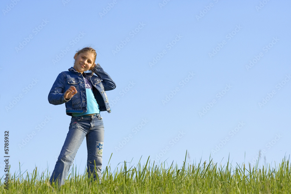 Girl costs on a grass on a background of the blue sky