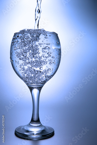 Clear liquid pour into footed glass over blue background
