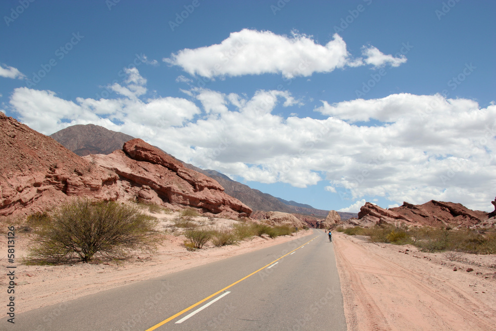 A lonely desert road with a few bicycle riders in the distance