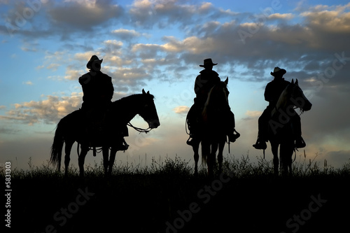 Three cowboys on horseback silhouetted against dawn sky