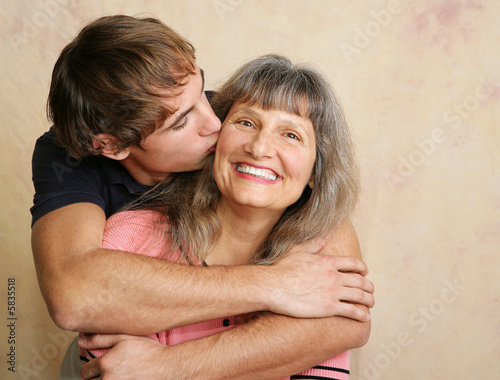 Young adult/late teen son kissing his mother on the cheek.