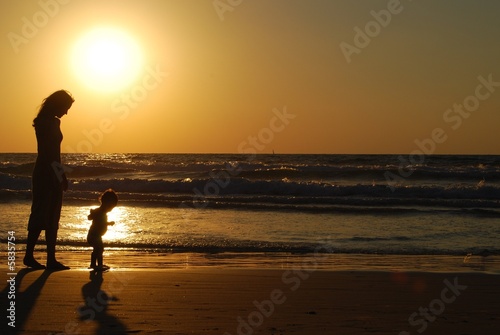 young woman with small child on the sea shore on sunset