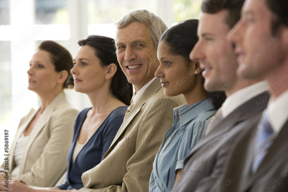 Confident mature businessman with team seated in line with him Confident mature businessman with team seated in line with him