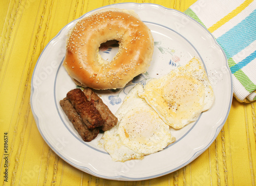 Eggs over easy, sausage and buttered bagel on yellow mat