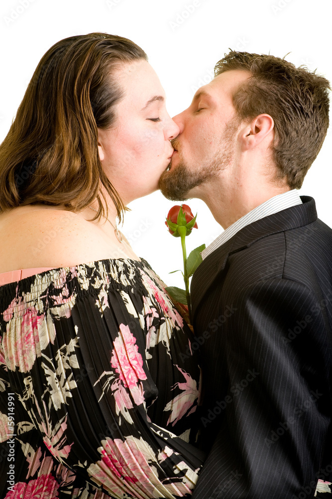 A young couple kissing while holding a single red rose. A young couple kissing while holding a single red rose.