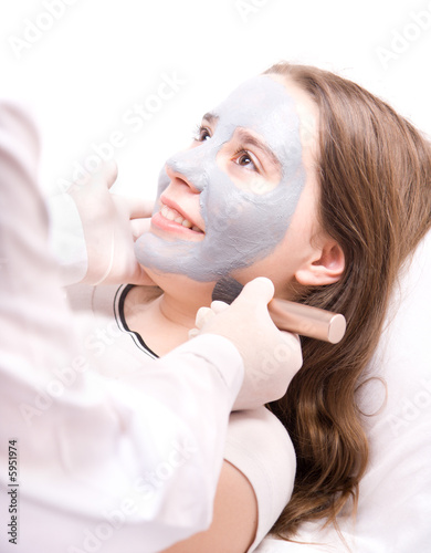 Beautician applying a clay mask on face young woman