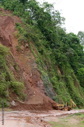 A backhoe moves dirt and mud from a mudslide along a highway