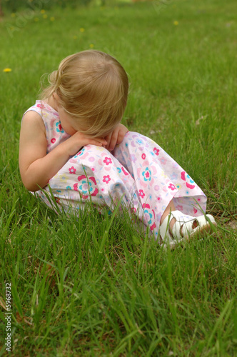 A preschool girl in a dress looking sad.