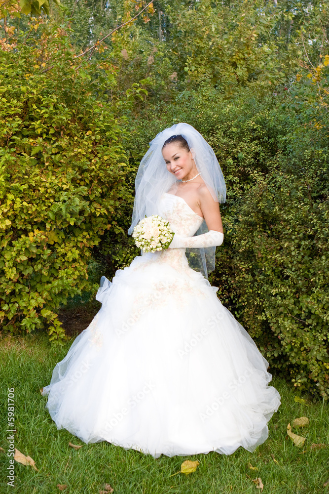 a smiling happy bride with a flower bouquet in the green lawn