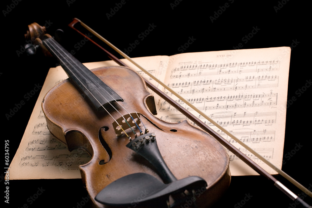Naklejka premium old violin with fiddlestick on music sheet isolated on black