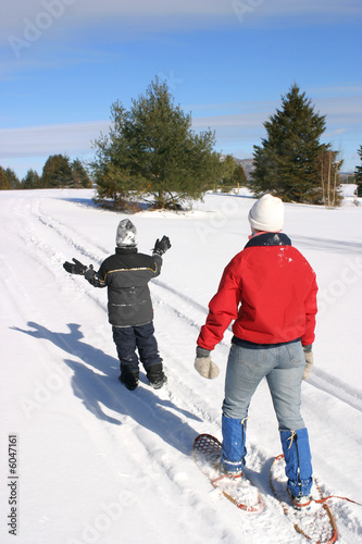 Adult and child snowshoeing across a wintry landscape.
