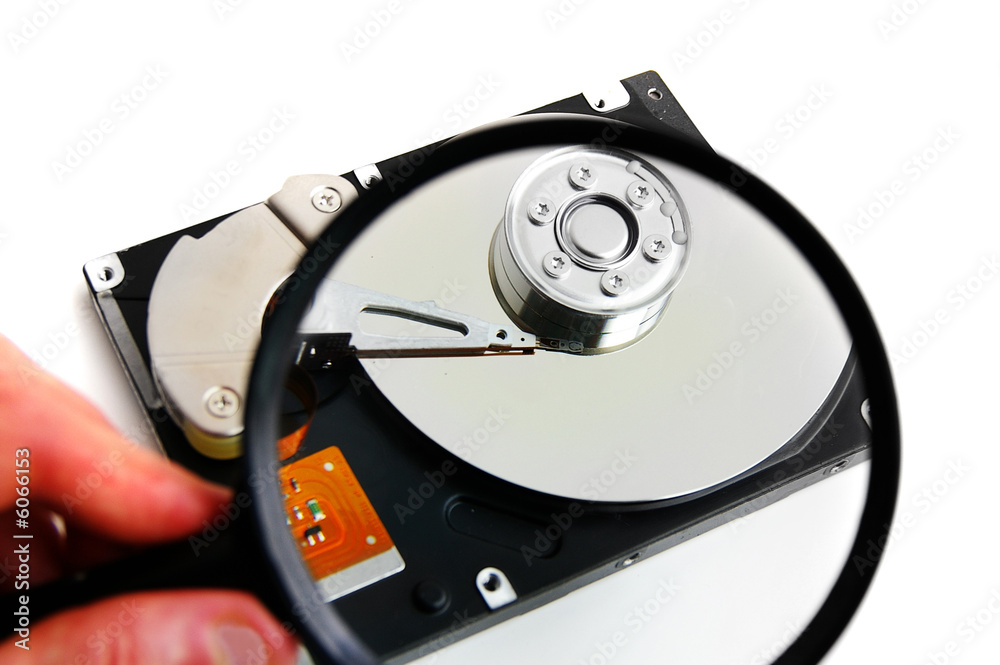 Hand holding a magnifying glass over a computer harddrive Hand holding a magnifying glass over a computer harddrive