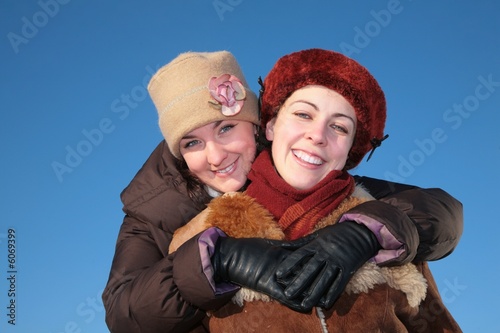 young woman embraces other against blue sky in winter