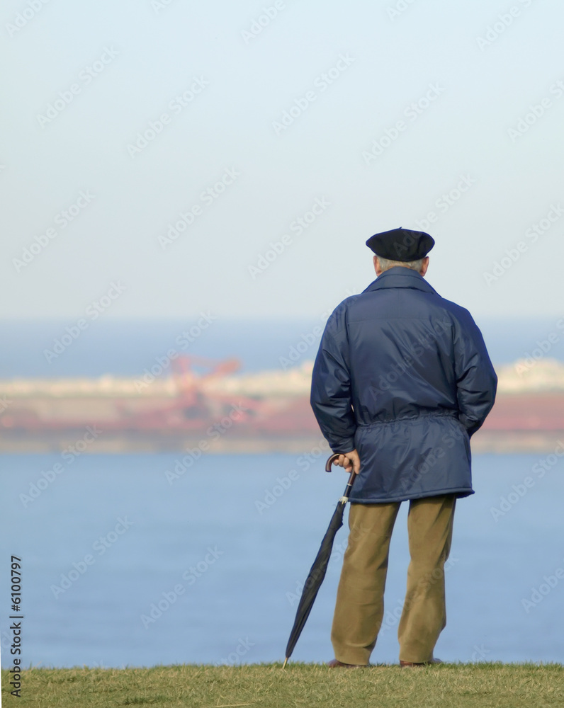 Hombre con paraguas y boina mirando al mar