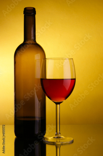 Glass of red wine and bottle over yellow background
