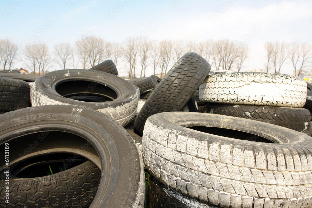 Heap of used car tires with trees in the background Heap of used car tires with trees in the background