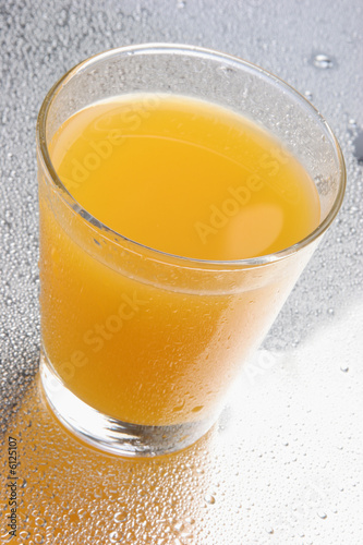 Orange juice on glass with drops on reflecting background