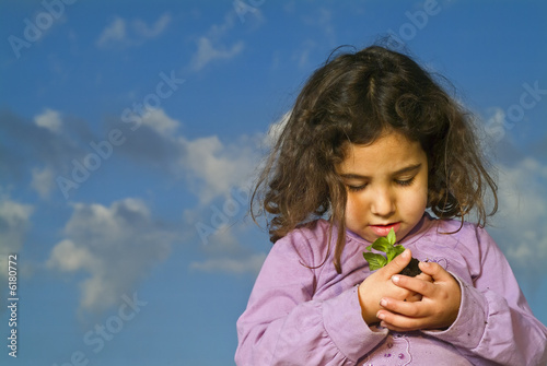 little girl holdinga plant against cludy blue sky