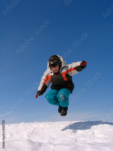 Boy jumping over snow on blue sky.