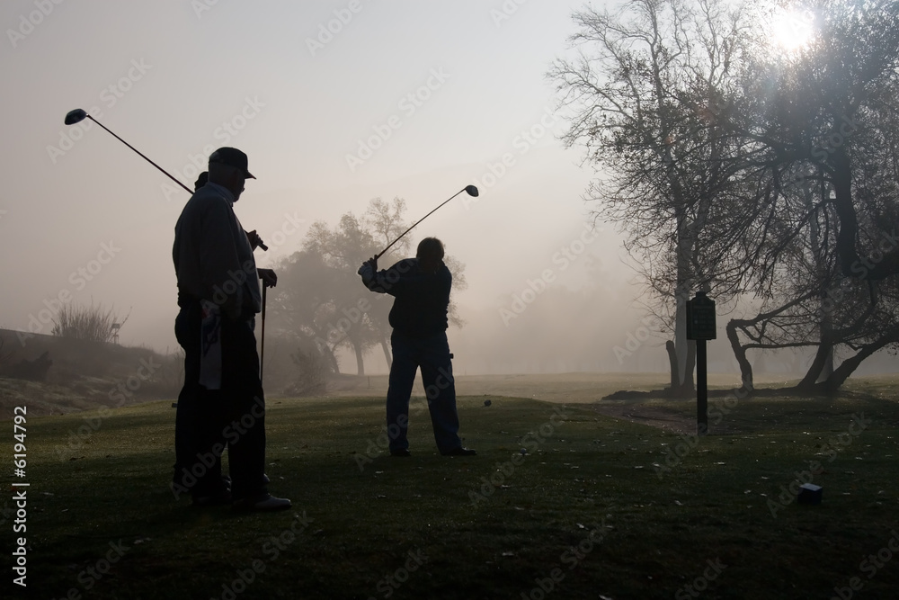 Early morning golfers silhouetted in a dense fog