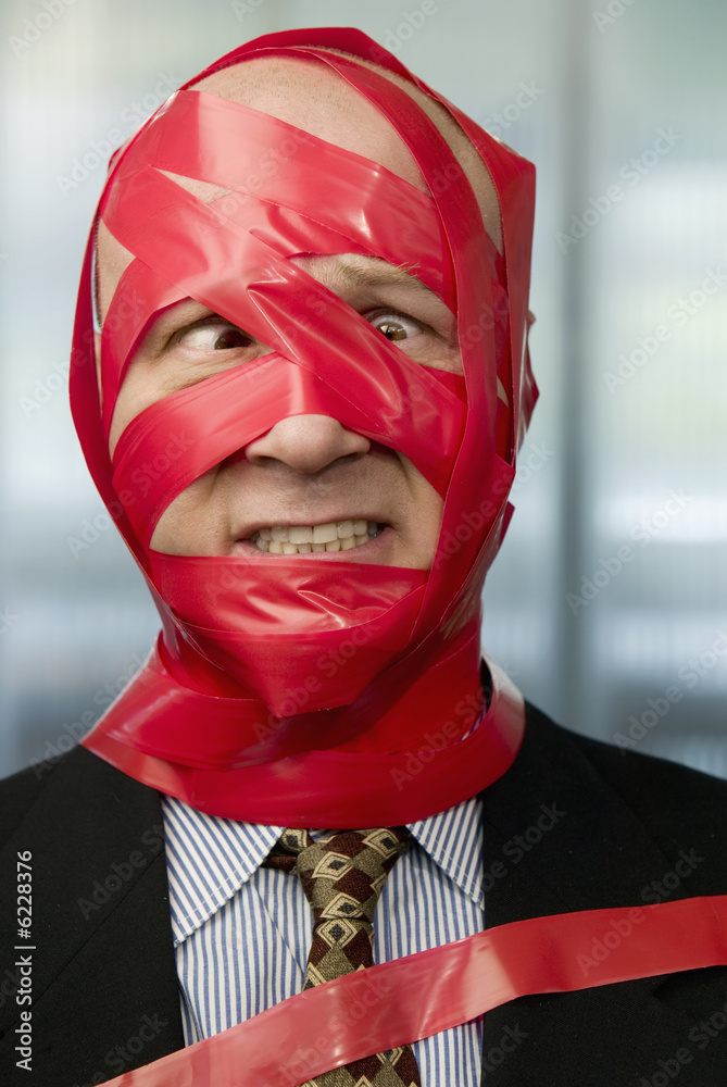 Cross-eyed businessman wrapped in red tape Cross-eyed businessman wrapped in red tape