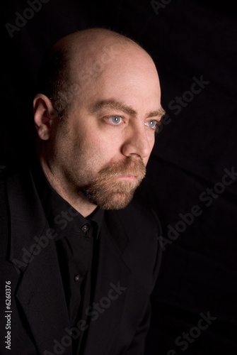 Man wearing a dark shirt and jacket over a black background