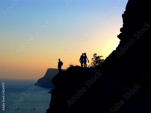 Three silhouettes on the cliff against the sunset background