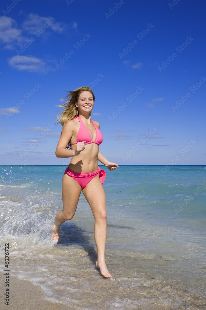 Beautiful Caucasian female teenage running through to surf