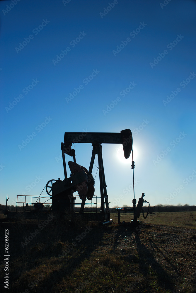 Silhouette of pump jack against the afternoon sun.