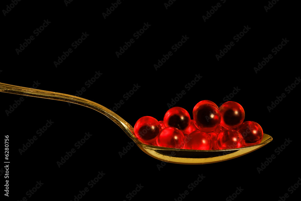 Fototapeta premium Red pills in a teaspoon, close-up, isolated on black